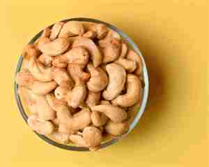 Nueces ricas en proteínas: plato de anacardos sobre fondo amarillo