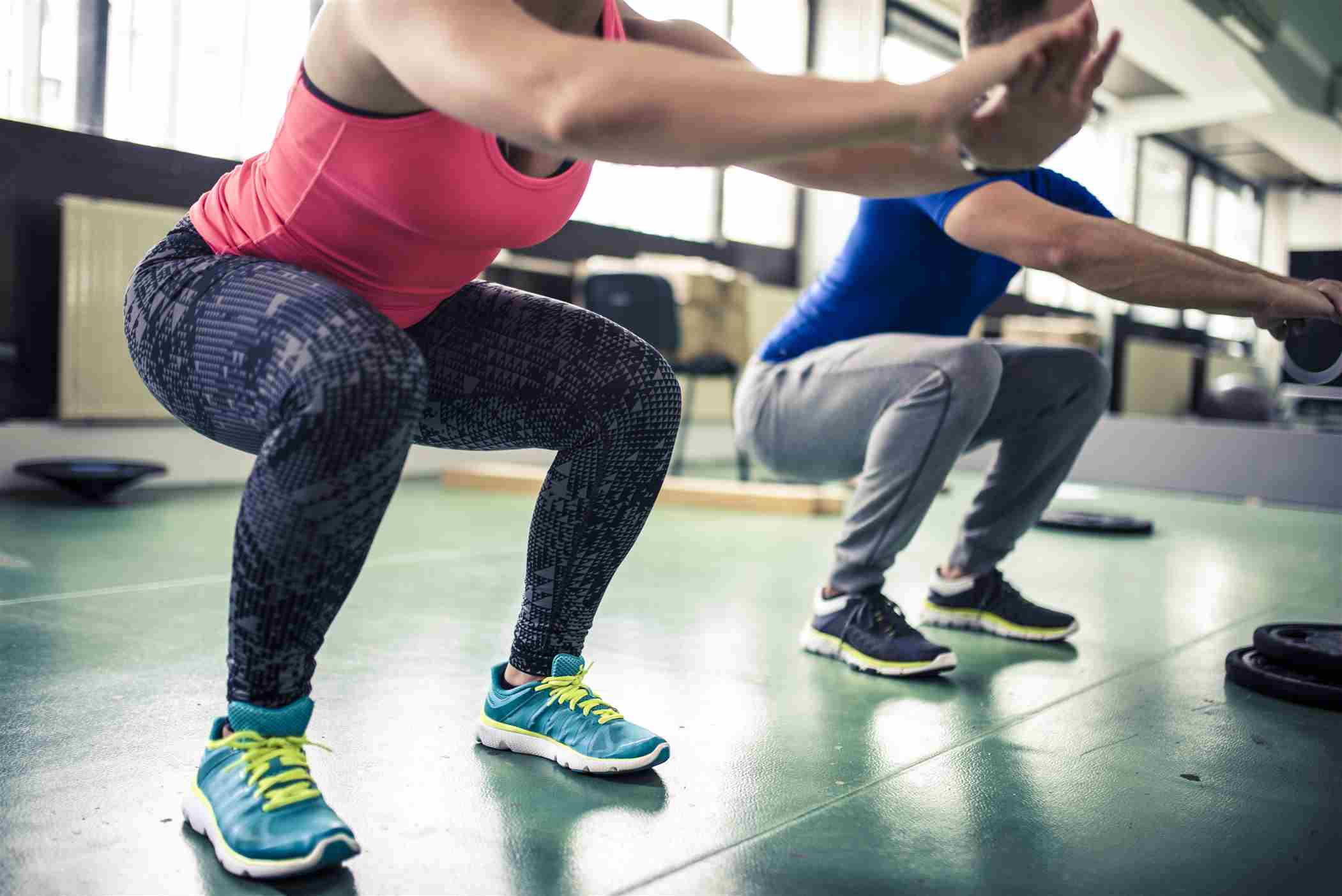 Una mujer y un hombre realizan ejercicios de sentadillas en un gimnasio.