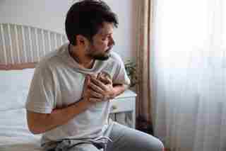 Proporcionado por Verywell Health Hombre con dolor en el pecho en la cama