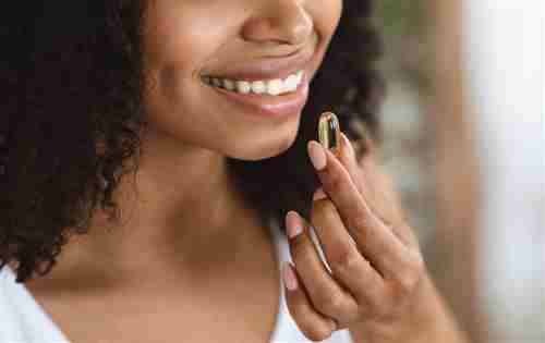 Proporcionado por The Hearty Soul Suplemento de belleza. Primer plano de una mujer negra sonriente tomando una cápsula de píldora de vitamina, teniendo nutrición dietética, imagen recortada