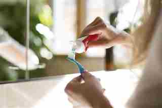 Una mujer poniendo pasta dental con flúor en un cepillo de dientes.