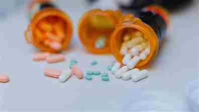 Timnewman / iStock vía Getty Images Plus Tres frascos abiertos de pastillas volteados para esparcir diferentes tipos de pastillas sobre el mostrador.