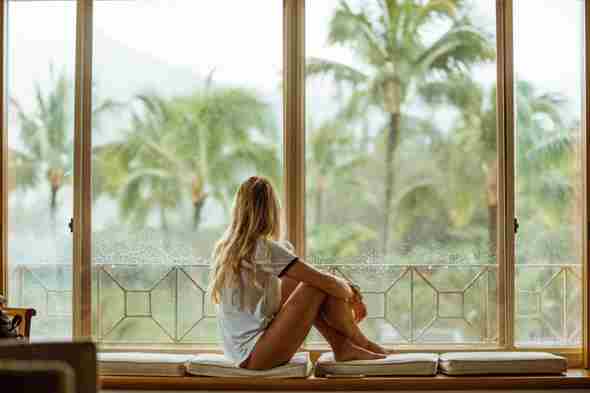 Proporcionado por Autoridad Orgánica mujer sentada en la ventana mirando las palmeras